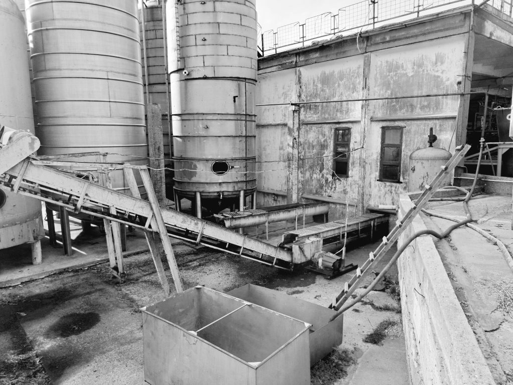 Black and white photo of an industrial warehouse featuring large silos and machinery.